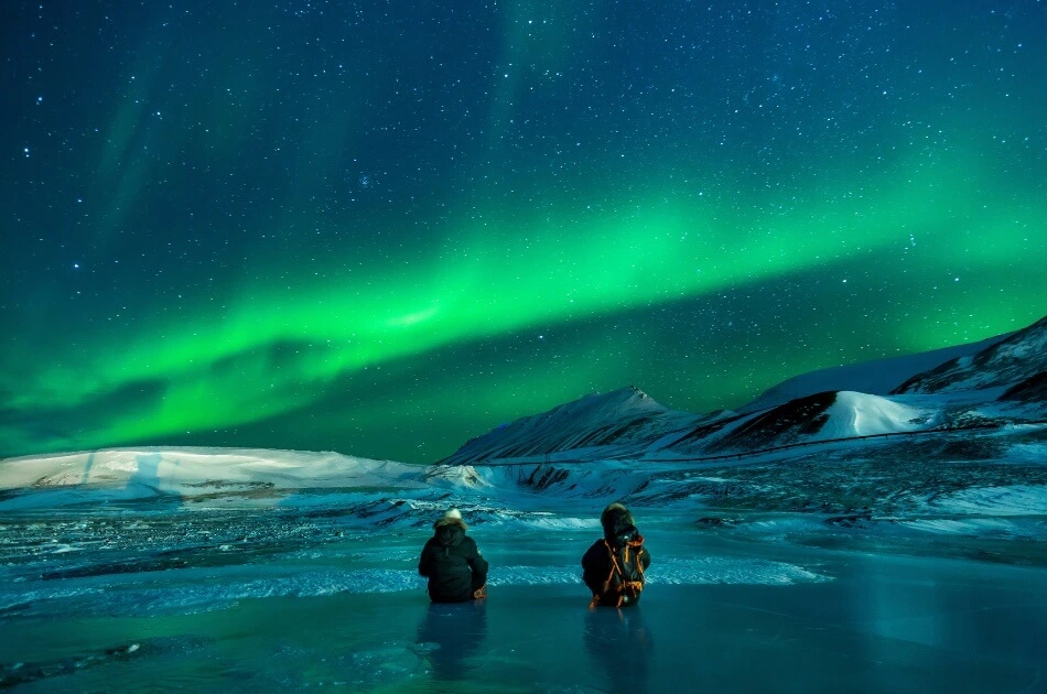 Travelers watching Northern Lights over snowy mountains in Iceland